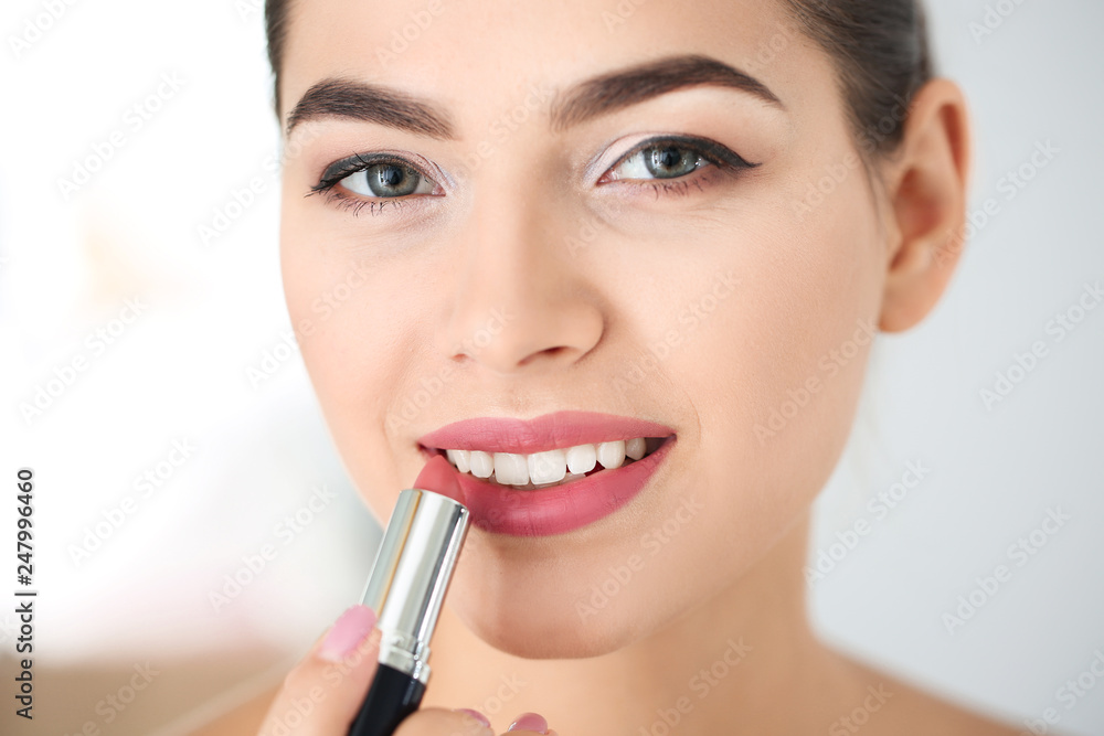 Young woman applying lipstick on blurred background