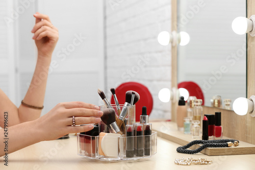 Woman reaching for organizer with cosmetic products and makeup accessories on dressing table indoors  closeup
