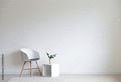 Stylish chair with shelf near white wall in room photo