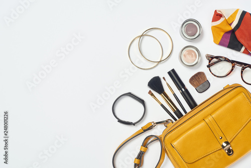 Top view of bracelets, scarf, glasses, mascara, cosmetic brushes, eye shadow and bag on white background