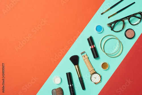 Mascara, watch, lipstick, bracelets, eye shadow, blush, glasses and cosmetic brushes on turquoise background