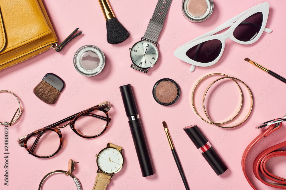 Top view of watches, lipstick, earrings, glasses, sunglasses, bag, eye shadow, blush, belt, cosmetic brushes, bracelets and mascara Top view of watches, lipstick, earrings, glasses, sunglasses, bag, eye shadow, blush, belt, cosmetic brushes, bracelets and mascara