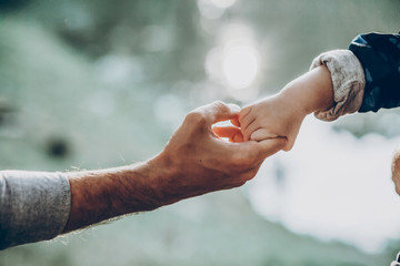 Father and son holding hands outdoors close-up, cute strong dad holding child's arm, parenting and trust concept