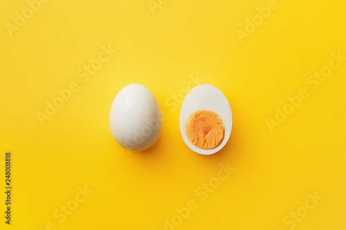 Foto Single whole white egg and halved boiled egg with yolk on a yellow background