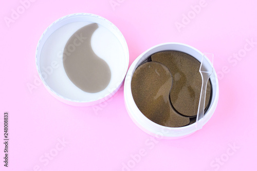 Round white container with black golden anti aging collagen lifting patches under eyes for woman face care with selective focus on pink neutral background. Hydrating beauty facial anti wrinkles patch