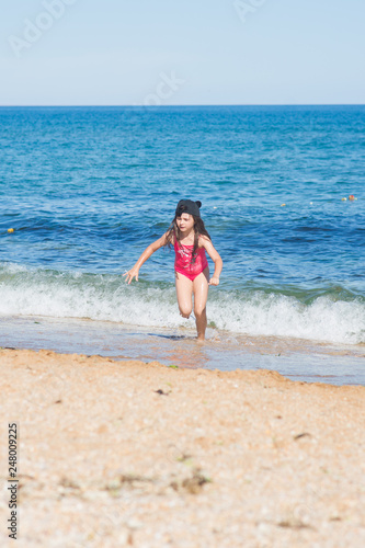 a little girl in a red swimsuit and a black cap dancing on the sandy beach