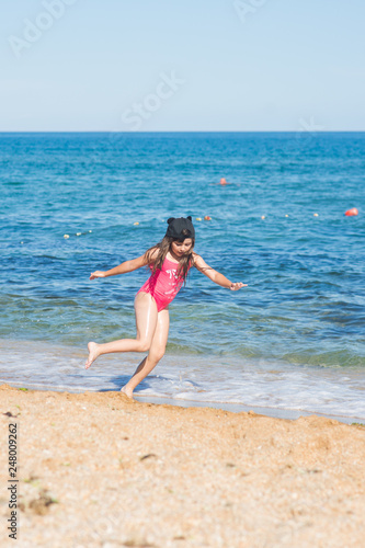 a little girl in a red swimsuit and a black cap dancing on the sandy beach