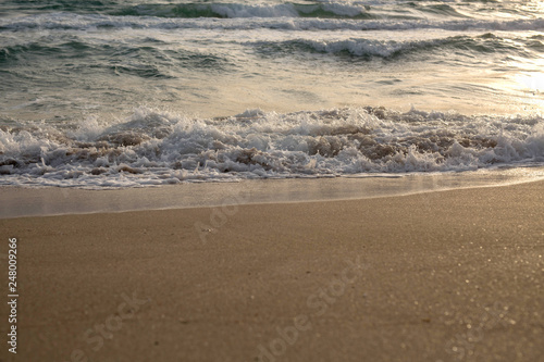 Scenic view of the waves of the blue sea on the sandy shore. Wild nature. Storm. Sunset on the sea.