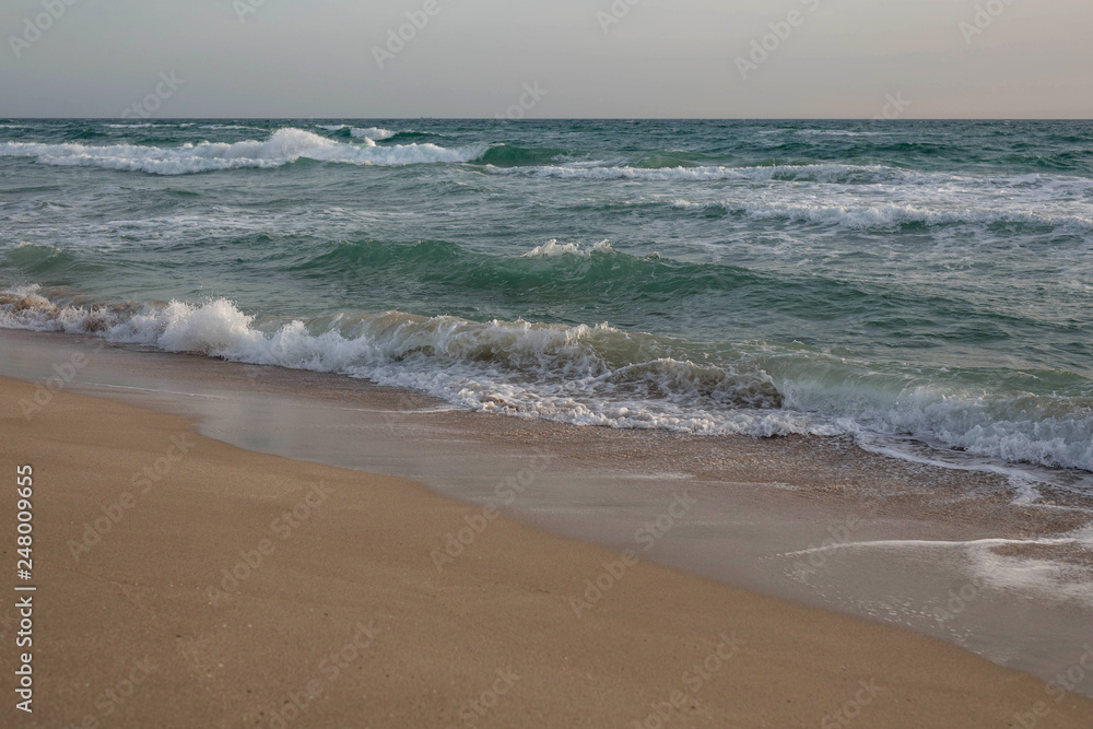 Scenic view of the waves of the blue sea on the sandy shore.
Wild nature. Storm. Sunset on the sea.