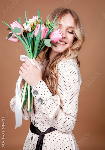 Happy beautiful woman with bouquet of spring tulips smilling over beige background.