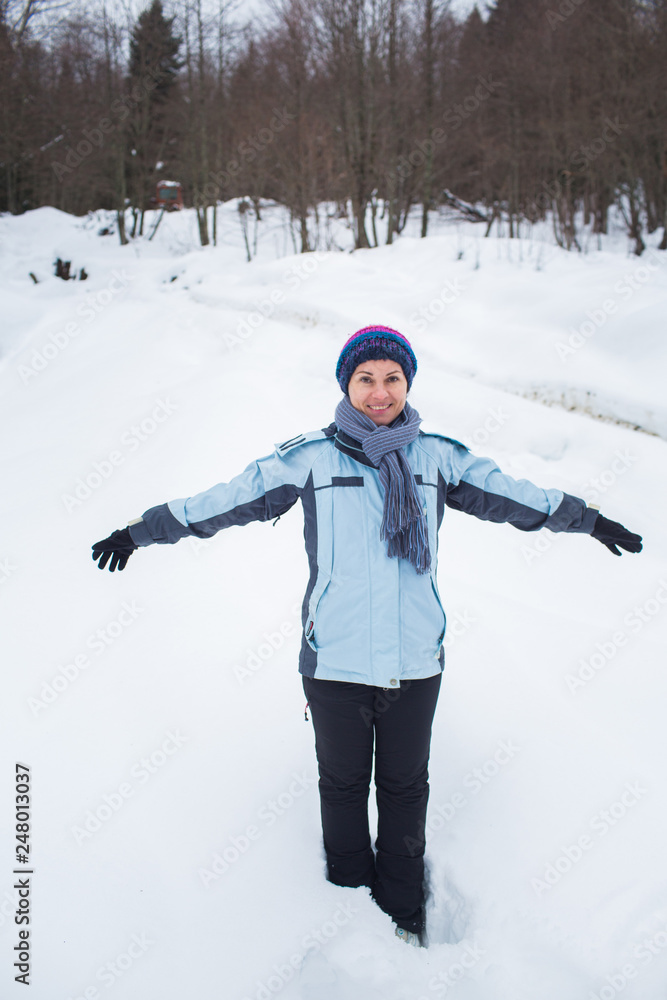 girl in pants, jacket, gloves and scarf standing in the snow in front of the forest arms out to the side