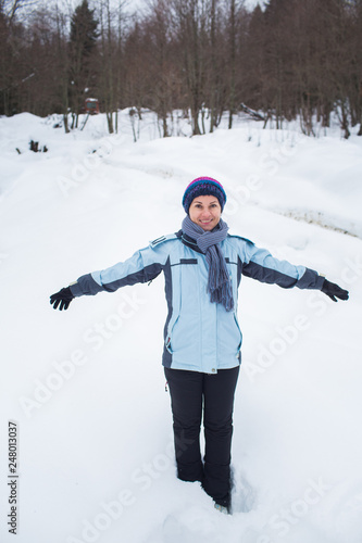 girl in pants, jacket, gloves and scarf standing in the snow in front of the forest arms out to the side