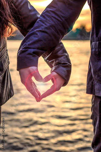 Mann und Frau formen aus ihren Händen ein Herz beim Sonnenuntergang am See, hochformat
