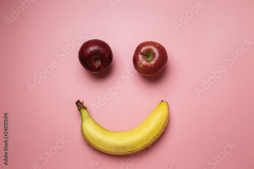 Smiley face with two apples and a banana with copy space on a pink background