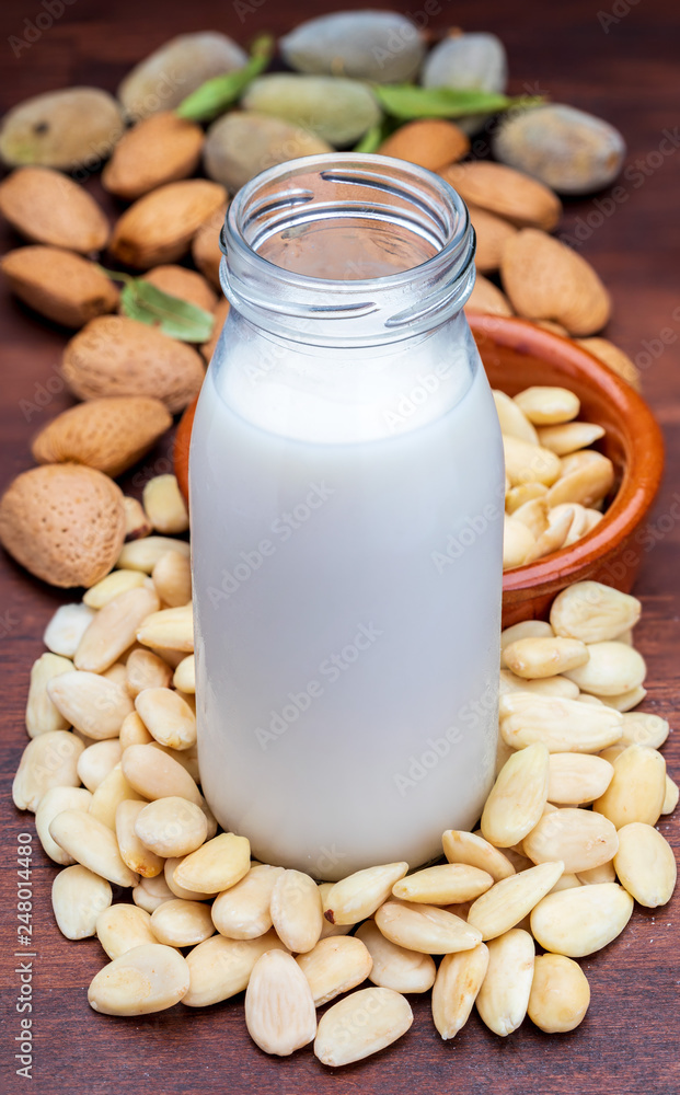 Almond milk in glass bottle. Includes peeled almonds. On rustic wooden background. Almond milk in glass bottle. Includes peeled almonds. On rustic wooden background.
