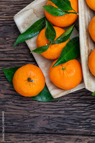 Fresh and raw tangerines with green leaves. Rustic appearance. On wooden background.