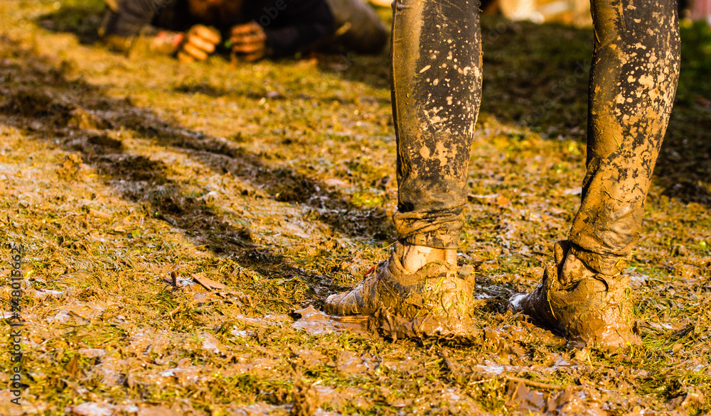 Mud race runners passing under a barbed wire obstacles during extreme obstacle race,detail of legs Mud race runners passing under a barbed wire obstacles during extreme obstacle race,detail of legs