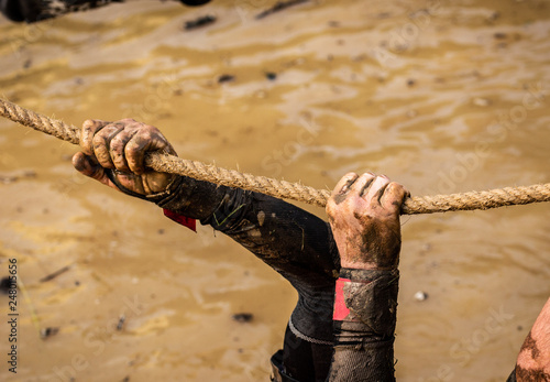 Mud race runners, defeating obstacles by using ropes. Details of the hands.