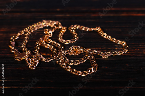 Golden chain weaving non, on wood background. Macro, soft focus.