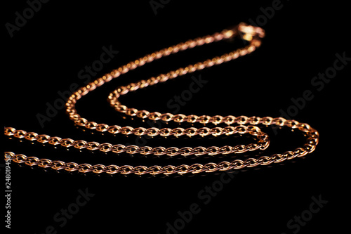 Golden chain weaving non, on a black background with reflection. Isolate, macro, soft focus.