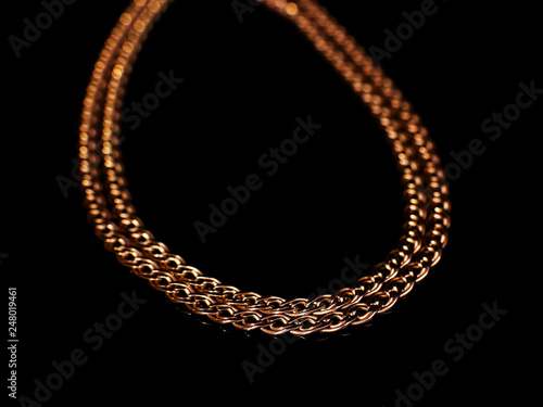 Golden chain weaving non, on a black background with reflection. Isolate, macro, soft focus.