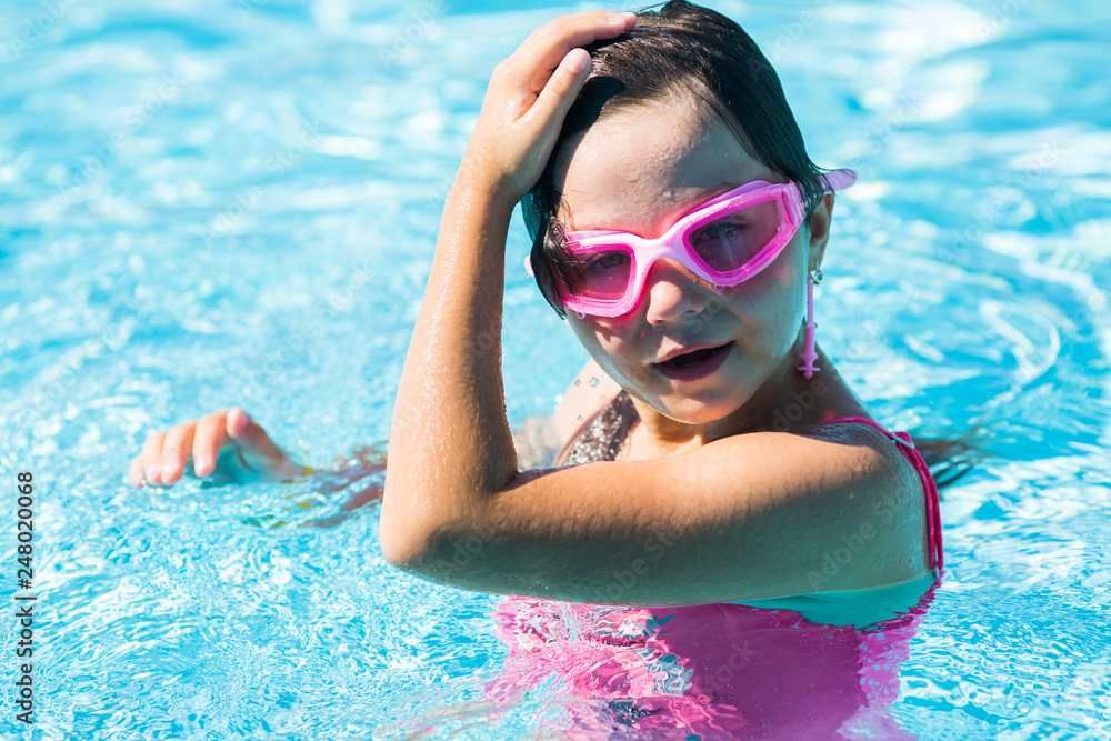 a little girl in a pink swimming mask in the pool straightens her hair