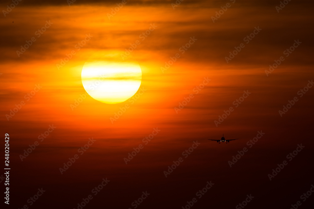 Airplane silhouette in the sunset with red sky and big sun