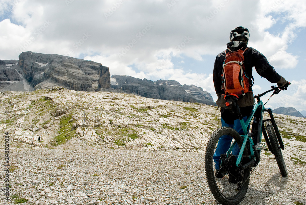 man with electric bike, e-bike, ebike, mtb, observes Cima Grostè Peak, Dolomites mountains, unesco heritage, Madonna di Campiglio, summer, sport, adventure, travel, Alps, Trentino, Alto Adige, Italy