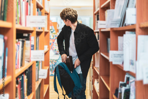 Foto young man trying to steal book from the library. kleptomania b