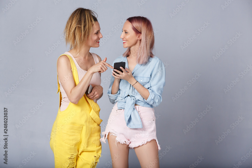 Φωτογραφία Two cute girlfriends communicate on the theme of applications in the smartphone holding them in hands