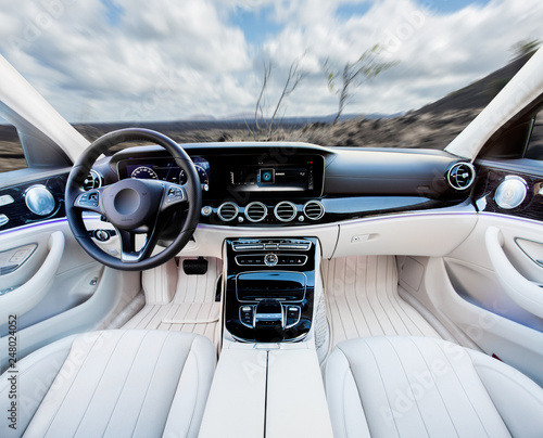 Dark car Interior - steering wheel, shift lever and dashboard. Car modern inside. Front view on sunset and sea background. The sun shines in the glass.glare