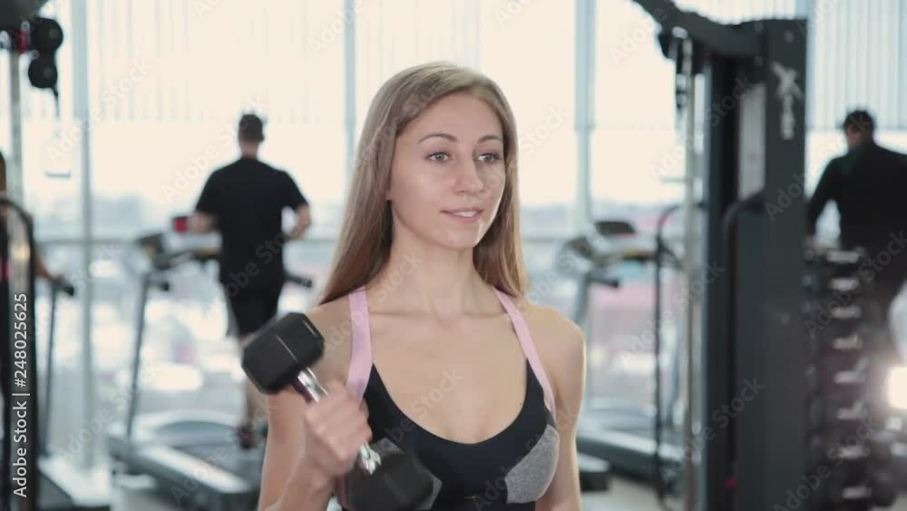 Beautiful athletic young girl trains dumbbells biceps in the gym. Beautiful athletic young girl trains dumbbells biceps in the gym.