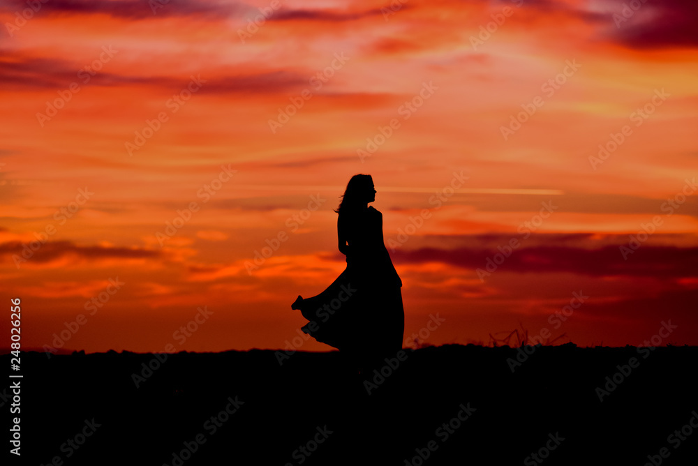 Silhouette of young woman with long dress at sunrise  on the beach 