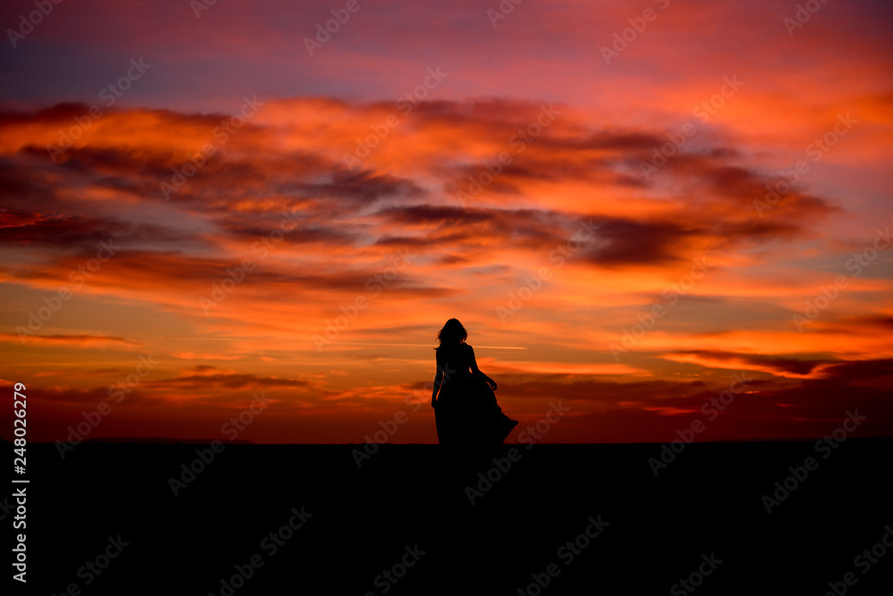 Silhouette of a young woman with long dress at sunset 