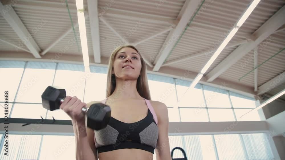 Beautiful athletic young girl trains dumbbells biceps in the gym. Beautiful athletic young girl trains dumbbells biceps in the gym.