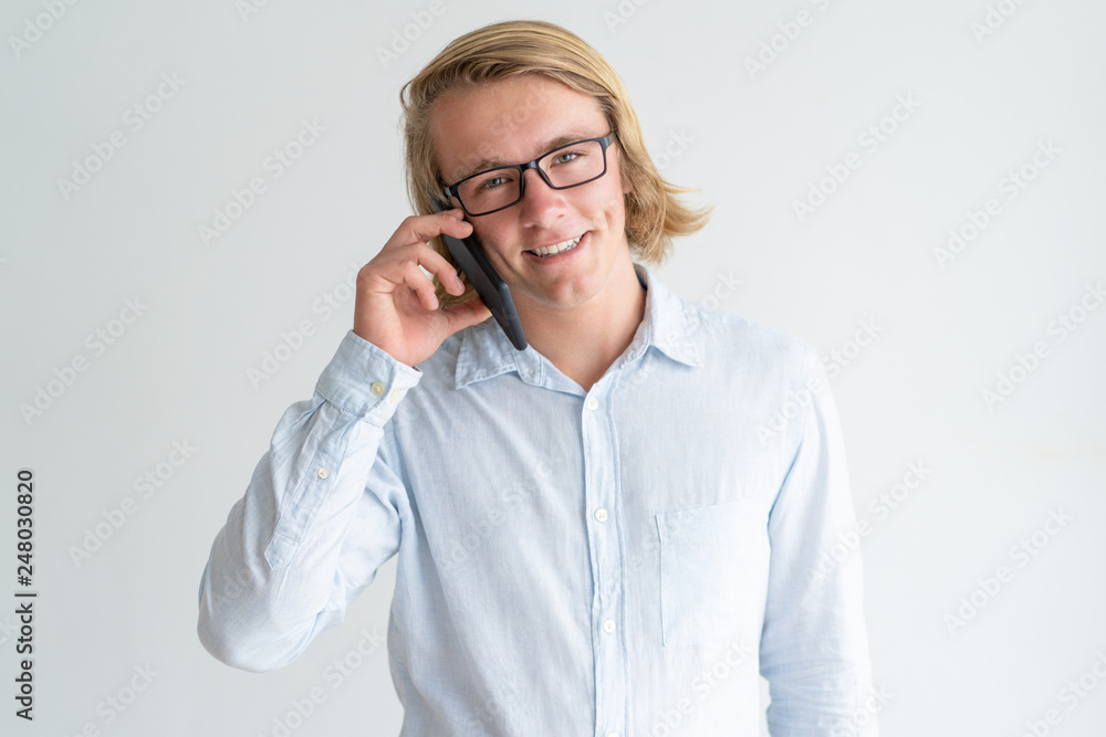 Smiling young man talking on smartphone and looking at camera