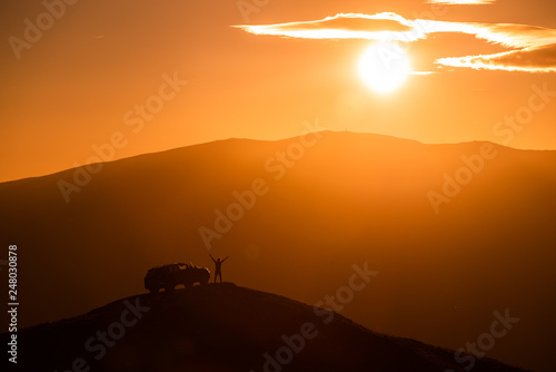 Silhouette of travel adventurer with off road car on top of the mountain 