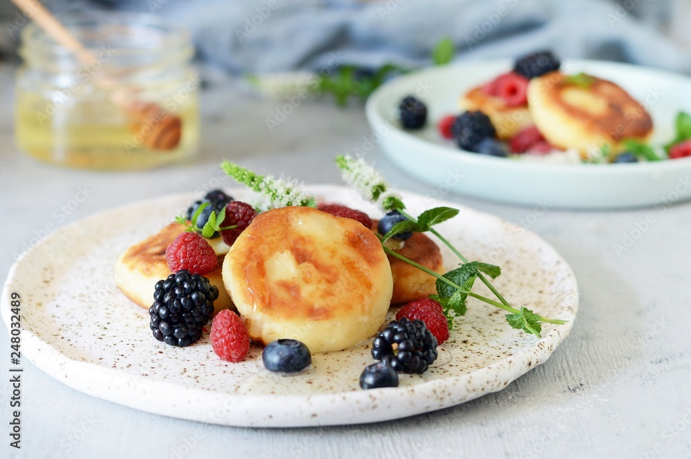 Sunday breakfast with cheesecake, honey, fresh berries and mint. Cottage cheese pancakes or curd fritters decorated honey and berries in plate on blue table top view. Healthy and diet breakfast. Sunday breakfast with cheesecake, honey, fresh berries and mint. Cottage cheese pancakes or curd fritters decorated honey and berries in plate on blue table top view. Healthy and diet breakfast.