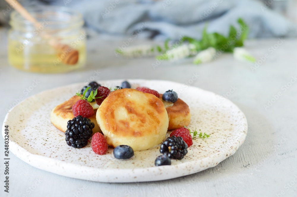 Sunday breakfast with cheesecake, honey, fresh berries and mint. Cottage cheese pancakes or curd fritters decorated honey and berries in plate on blue table top view. Healthy and diet breakfast. Sunday breakfast with cheesecake, honey, fresh berries and mint. Cottage cheese pancakes or curd fritters decorated honey and berries in plate on blue table top view. Healthy and diet breakfast.