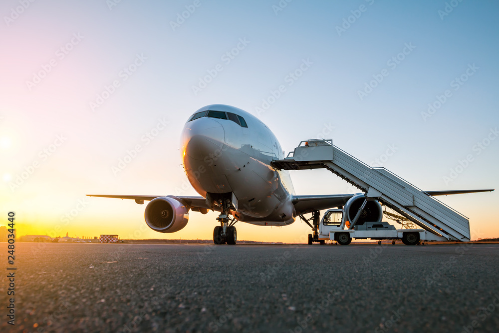 White wide body passenger aircraft with a boarding steps at the airport apron in the evening sun White wide body passenger aircraft with a boarding steps at the airport apron in the evening sun