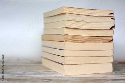 Stack of yellowed old used paperback books on wood desk and light blue background