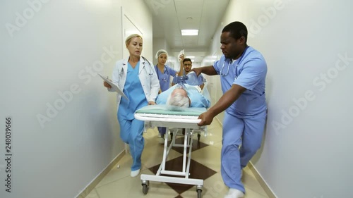 Dolly shot of team of professional ER medical personnel rushing critical elderly patient to surgery photo