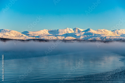 steam rising from the lake and snow-covered mountains, Lofoten Islands, Norway