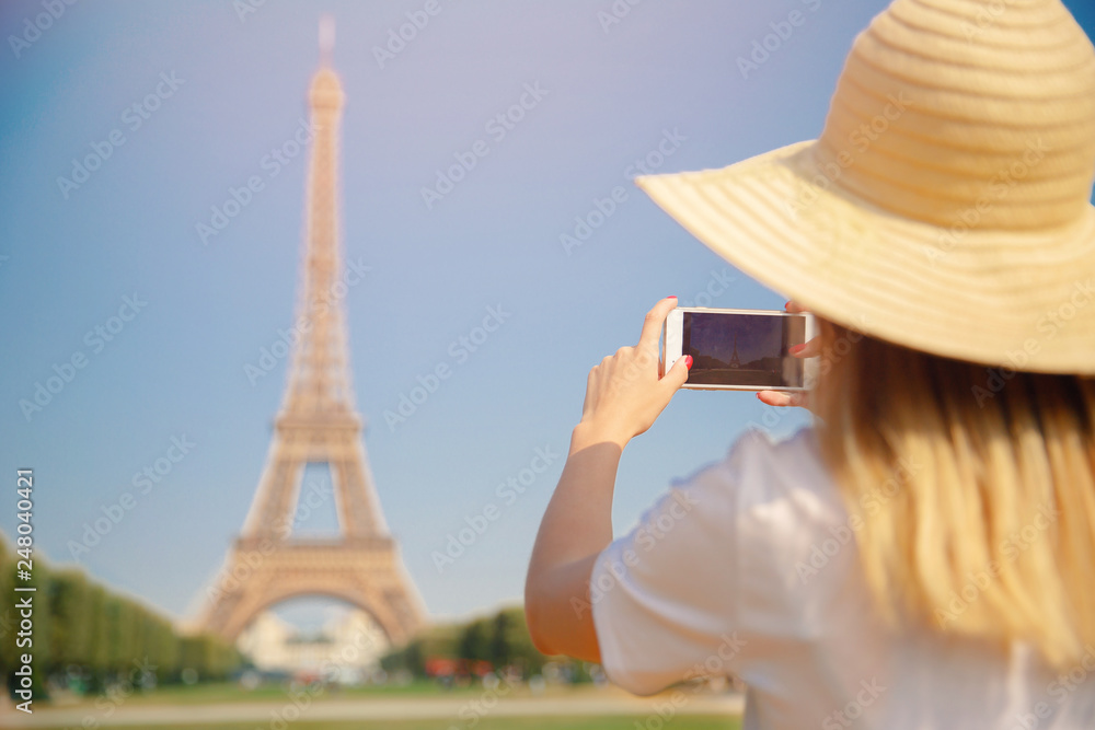 Travel blogger young woman in hat takes photograph of Eiffel Tower on telephone in Paris, France