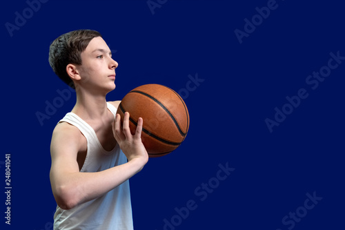 Basketball and teenager. The guy in the white jacket can throw a ball from the chest. Isolated on blue background. Copy space. Template for poster design or news about teenage basketball. © romsvetnik