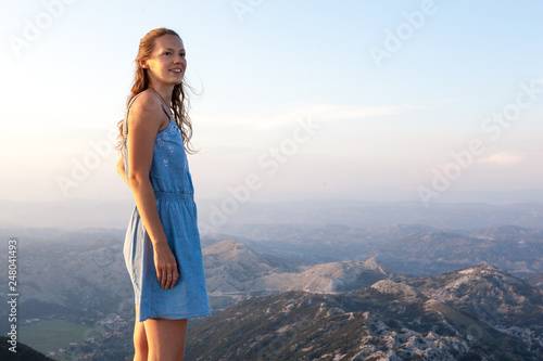 Beautiful girl tourist stands on top of a cliff and admires the beautiful landscape of the mountain range in Montenegro . Tourism, Travel and summer holiday concept