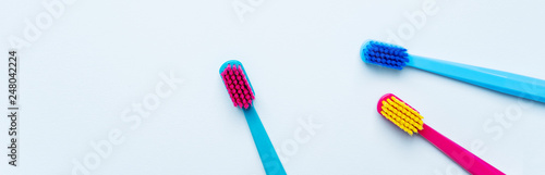 Colorful tooth brushes with bright color bristles on a light pastel blue background. Long wide banner for your mock up with dental tools and empty space for text.