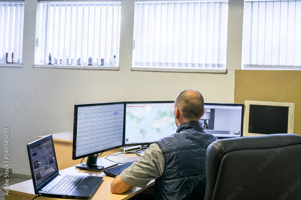 Monitoring department of a network Internet provider. A man looks at several monitors. Specialist in information security, view from the back Monitoring department of a network Internet provider. A man looks at several monitors. Specialist in information security, view from the back