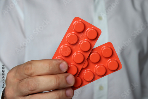 Doctor with pills in blister packs, man in white lab coat holding medication in orange tablets. Concept of vitamin C, prevention of flu, dose of drugs, pharmacy