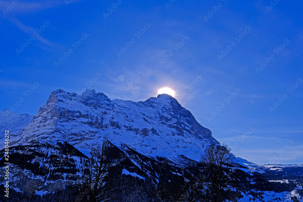 The sun hides behind the famous peak of the Eiger mountain above Grindelwald, with a lot of snow, Bern, Switzerland